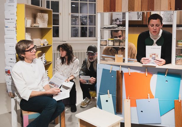 Gruppe von Menschen sitzt und steht in einem Raum mit Regalen und h&auml;lt Brosch&uuml;ren in der Hand