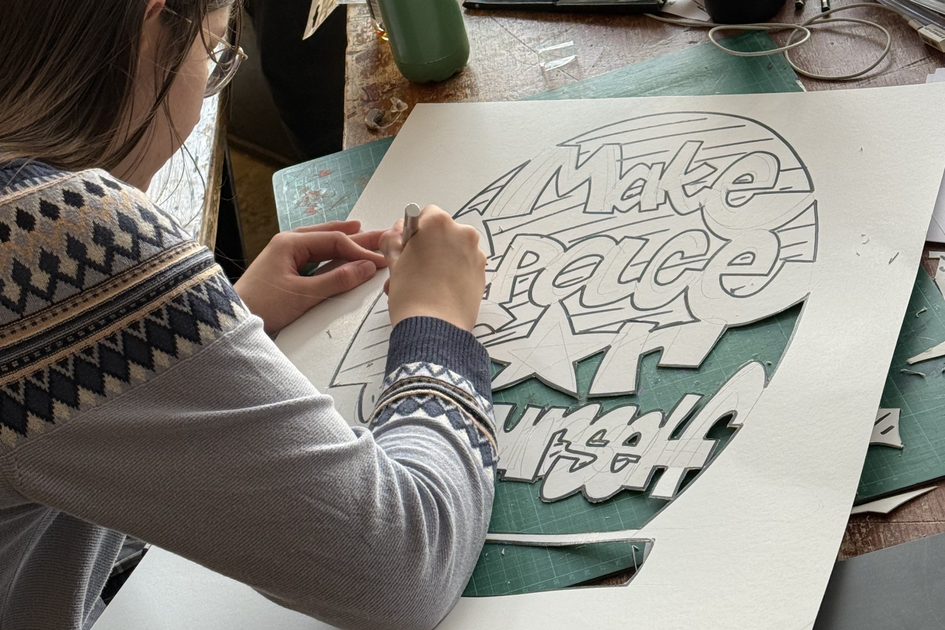 Blick von hinten über die Schulter einer Person, die gerade eine Schablone für ein Graffiti ausschneidet.